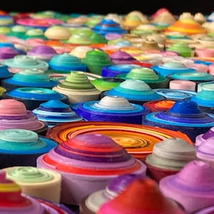 May include: Close-up of a colorful wall art piece made of layered paper circles. The circles are arranged in a random pattern and are in various shades of blue, green, purple, pink, orange, and yellow.