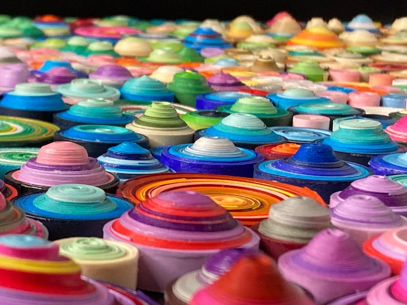 May include: Close-up of a colorful wall art piece made of layered paper circles. The circles are arranged in a random pattern and are in various shades of blue, green, purple, pink, orange, and yellow.
