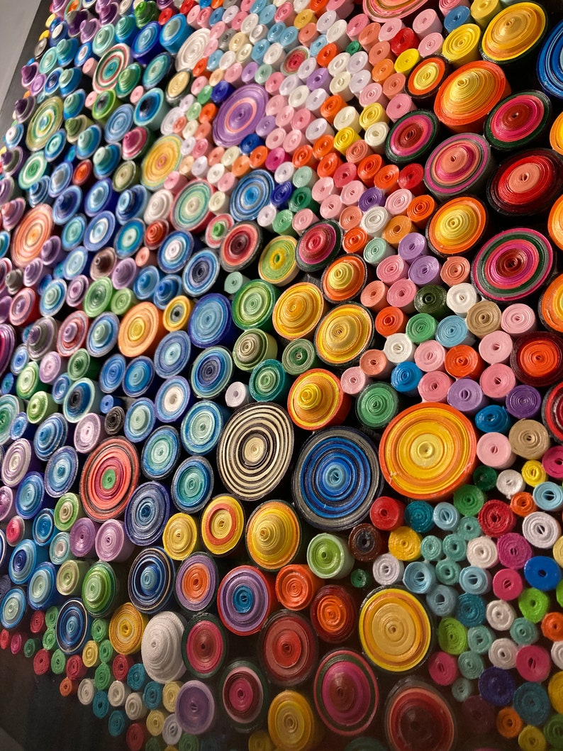 May include: A colorful wall art piece made of rolled paper circles in various sizes and colors. The circles are arranged in a pattern, creating a visually appealing and textured surface.