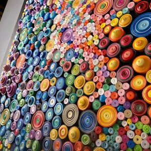 May include: A close-up of a colorful wall art piece made of rolled paper circles. The circles are arranged in a pattern and are in various shades of blue, green, yellow, orange, red, pink, and purple.