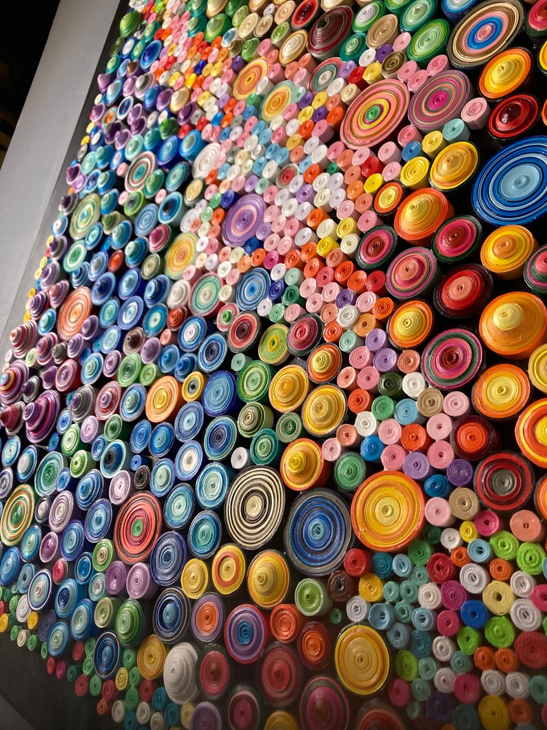 May include: A close-up of a colorful wall art piece made of rolled paper circles. The circles are arranged in a pattern and are in various shades of blue, green, yellow, orange, red, pink, and purple.