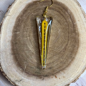 May include: A gold earring with a clear triangular resin pendant containing a yellow geometric design.