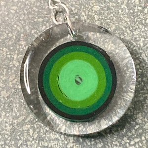 May include: Green and black paper quilling art encased in a clear round glass pendant with a silver hook earring.
