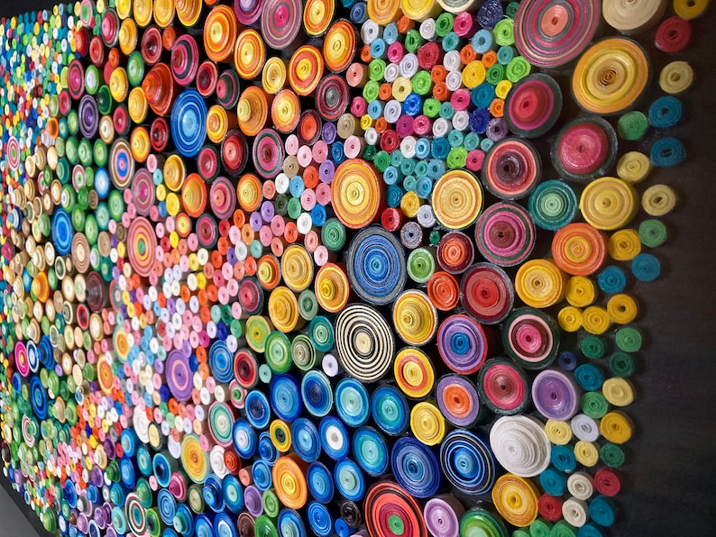 May include: A colorful wall art piece made of rolled paper circles in various sizes and colors. The circles are arranged in a random pattern, creating a visually appealing and textured surface.