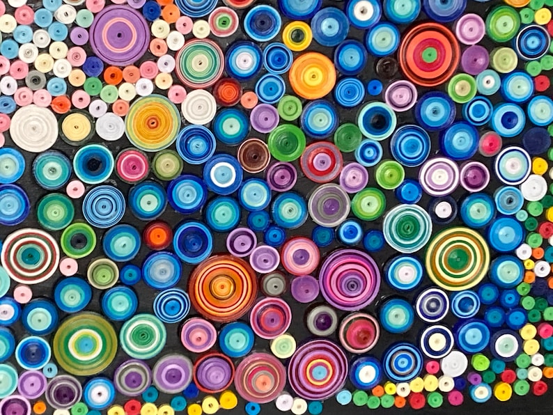 May include: A colorful abstract art piece made of paper circles of various sizes and colors. The circles are arranged in a random pattern on a black background.
