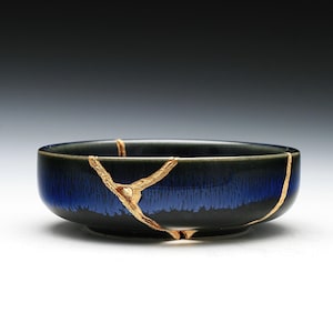 May include: A small, round bowl with a black and blue glaze. The bowl has gold cracks running through the glaze.
