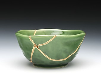 May include: A small, green ceramic bowl with a crackled glaze and gold accents. The bowl is slightly misshapen, giving it a unique and rustic look.