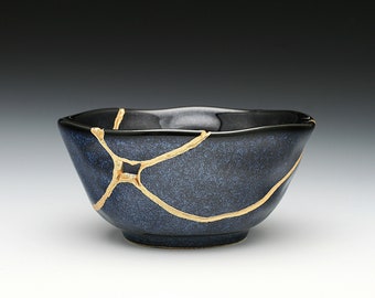 May include: A small, dark blue ceramic bowl with gold cracks. The bowl is slightly chipped and has a textured surface.