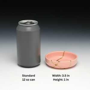 May include: A standard 12 oz aluminum can next to a small pink ceramic bowl with gold crackle lines. The bowl is 3.5 inches wide and 1 inch high.