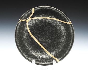 May include: A black ceramic bowl with gold cracks. The bowl has a speckled, textured surface.