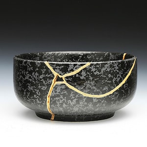 May include: A black ceramic bowl with a crackled glaze and gold accents. The bowl has a wide rim and a rounded bottom.