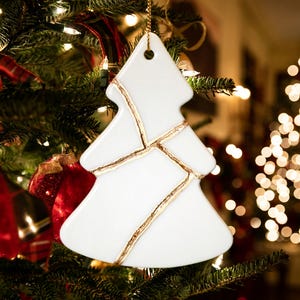 May include: White porcelain Christmas tree ornament with gold accents. The ornament is shaped like a Christmas tree and has a gold string for hanging.