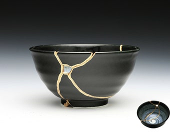 May include: A black ceramic bowl with gold cracks and a blue and white glaze. The bowl is a traditional Japanese style known as Kintsugi, which means "golden joinery".