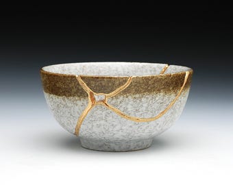 May include: A white ceramic bowl with a brown rim and gold cracks. The bowl is slightly chipped and has a rustic look.