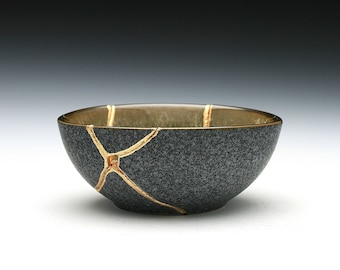May include: A small, dark gray ceramic bowl with gold cracks. The bowl is round and has a slightly flared rim.