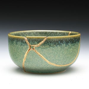 May include: A green ceramic bowl with gold cracks. The bowl is slightly chipped and has a textured surface.