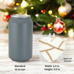 Peut inclure: Une d&eacute;coration en forme de c&oelig;ur blanche avec des accents dor&eacute;s, mesurant 7,6 cm de largeur et de hauteur. Une canette standard de 355 ml est pr&eacute;sent&eacute;e &agrave; titre de comparaison de taille. Le support n'est pas inclus.