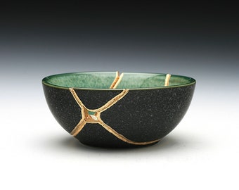 May include: A small, dark green ceramic bowl with gold cracks. The bowl is slightly chipped and has a speckled texture.