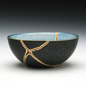 May include: A small, black ceramic bowl with a blue glaze inside. The bowl has gold cracks running through it.