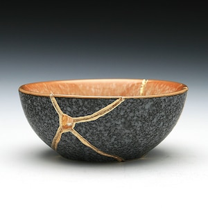 May include: A small, black ceramic bowl with a speckled finish. The bowl has a crackled glaze with gold accents.