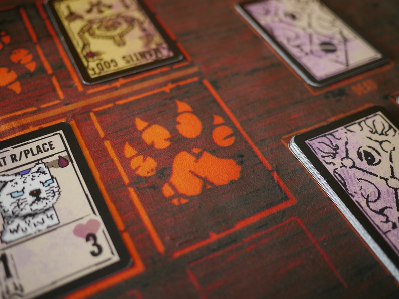 May include: A close-up of a game board with a red paw print in the centre. There are several cards on the board, including one with a white cat and the text "Cat R/Place".