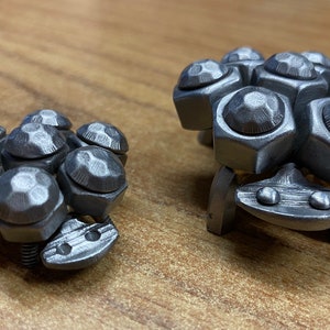 May include: Two silver metal sculptures of stylised creatures with multiple round, faceted, and textured protrusions. The larger sculpture has a flat base with two small round protrusions on the front.