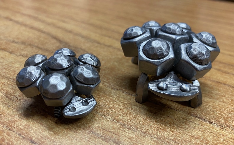 May include: Two silver metal sculptures of stylised creatures with multiple round, faceted, and textured protrusions. The larger sculpture has a flat base with two small round protrusions on the front.