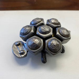 May include: A silver metal sculpture of a turtle made from hexagonal nuts. The turtle has six legs and a head made from metal.