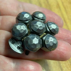 May include: A cluster of six silver-toned metal knobs with a hexagonal base and a rounded top. The knobs are arranged in a circular pattern and are connected by a silver-toned metal screw.