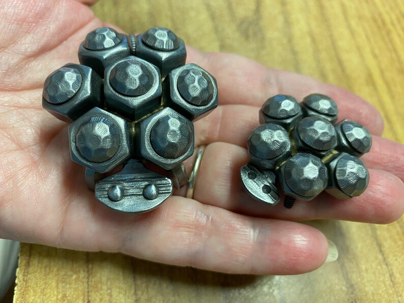 May include: Two silver metal rings with a cluster of hexagonal shaped pieces. The larger ring has 7 pieces and the smaller ring has 6 pieces.