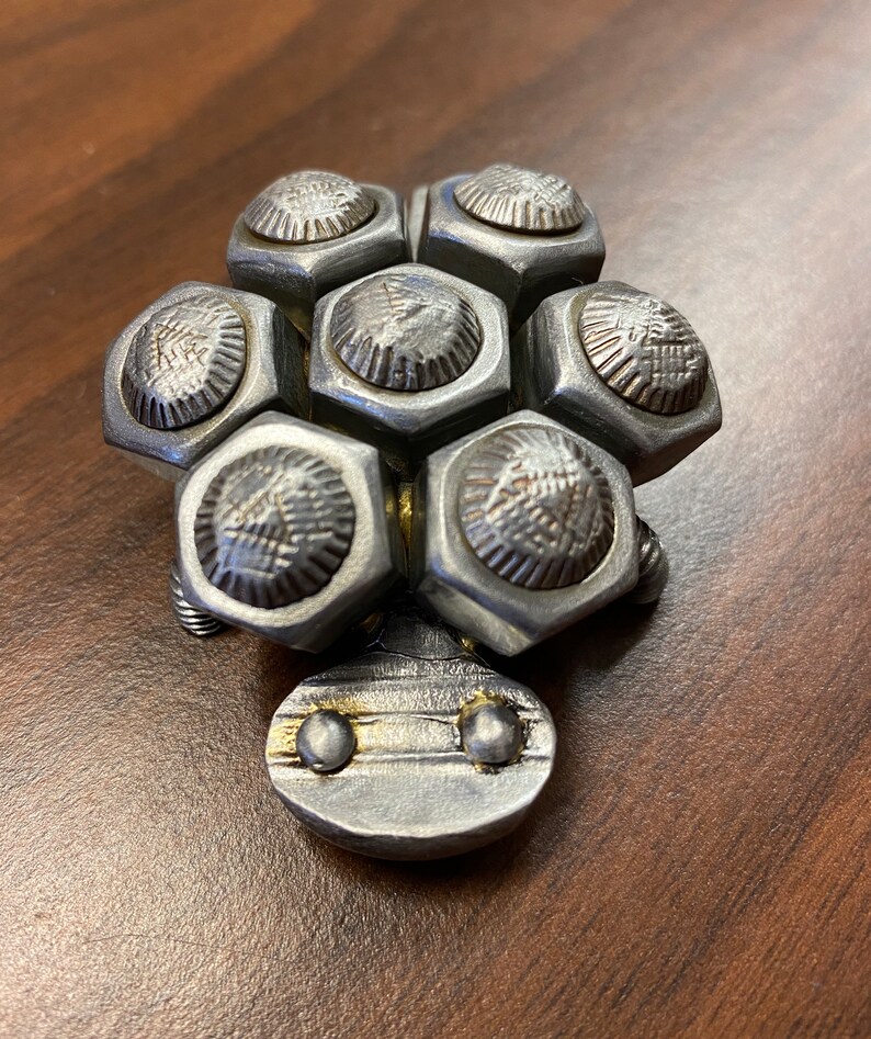 May include: A small metal turtle sculpture made from nuts and bolts. The turtle is silver with a gold accent on the head.