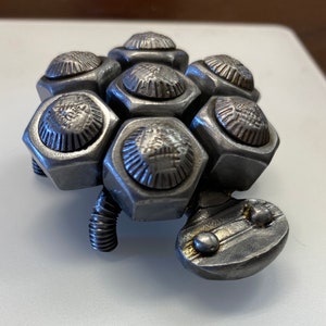 May include: A silver metal sculpture of a turtle made from nuts and bolts. The turtle has a detailed shell and a small head.