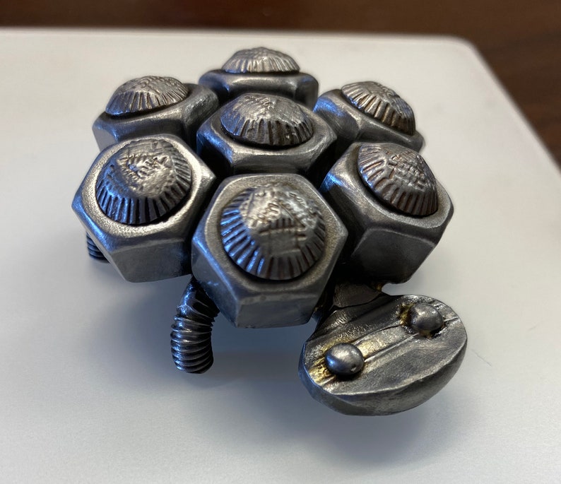 May include: A silver metal sculpture of a turtle made from nuts and bolts. The turtle has a detailed shell and a small head.