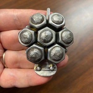 May include: A silver metal sculpture of a flower with a hexagonal design. The flower is made of multiple small, round, silver metal pieces that are connected together.
