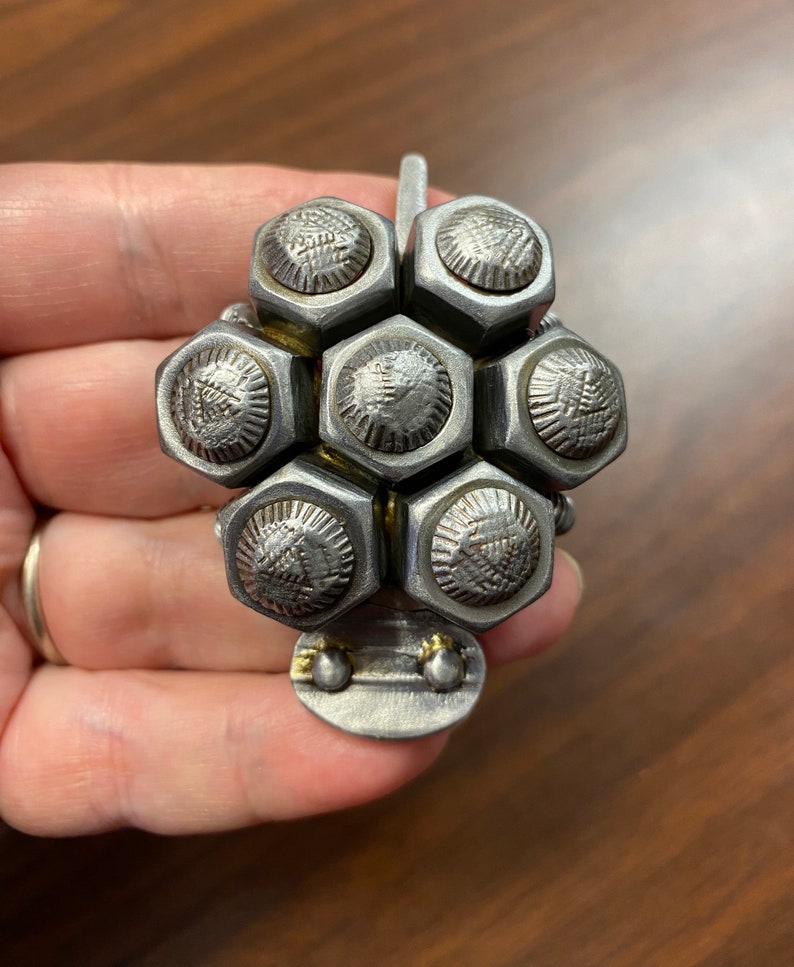 May include: A silver metal sculpture of a flower with a hexagonal design. The flower is made of multiple small, round, silver metal pieces that are connected together.