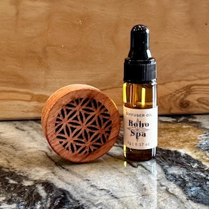May include: A small brown wooden diffuser with a geometric pattern and a clear glass bottle of diffuser oil labeled "Boho Spa" with a black dropper top.