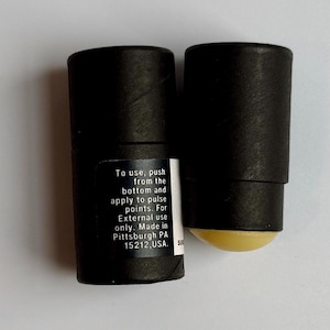 May include: Two black cylindrical containers, one with a yellow applicator visible. One container has a label with instructions: "To use, push from the bottom and apply to pulse points. For External use only. Made in Pittsburgh PA 15212, USA."