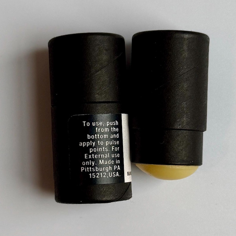 May include: Two black cylindrical containers, one with a yellow applicator visible. One container has a label with instructions: "To use, push from the bottom and apply to pulse points. For External use only. Made in Pittsburgh PA 15212, USA."