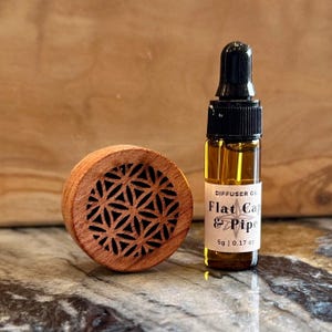 May include: A small brown wooden diffuser with a geometric pattern and a clear glass bottle of diffuser oil labeled "Flat Cap & Pipe" 5g | 0.17 oz.