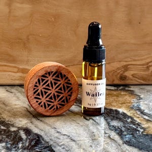 May include: A small brown wooden diffuser with a geometric pattern and a clear glass bottle of diffuser oil labeled "Wailea" with a star design. The bottle contains 5g or 0.17 oz of oil.