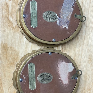 May include: Two gold-toned oval picture frames with ornate detailing. The back of each frame has a label with the text "A Cameo Creation" and the name of the person depicted in the portrait. The top frame has the text "Lady Sheffield" and the bottom frame has the text "Elizabeth, Duchess of Devonshire".