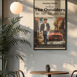 May include: A rectangular wall poster featuring the title The Outsiders by S.E. Hinton. The artwork displays a person in a dark jacket and blue jeans walking near a red car. Text includes character names, published 1969, and Get smart and nothing can touch you.