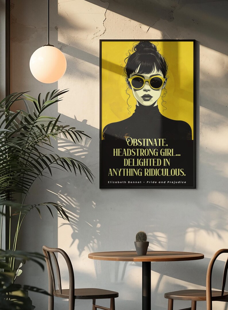 Puede incluir: Un cuadro enmarcado con una mujer con gafas de sol sobre un fondo amarillo. El cuadro incluye la cita "OBSTINATE, HEADSTRONG GIRL... DELIGHTED IN ANYTHING RIDICULOUS." de Elizabeth Bennet en Orgullo y Prejuicio. El cuadro est&aacute; en una habitaci&oacute;n.