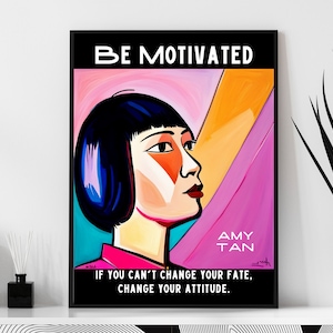 May include: A framed art print with the words "BE MOTIVATED" at the top. The artwork features a stylized portrait of a woman with black hair and a pink and orange background. The text "AMY TAN" and a motivational quote are also included.