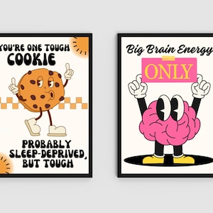 May include: Two framed art prints with black borders. One features a cartoon cookie with the text "YOU'RE ONE TOUGH COOKIE" and "PROBABLY SLEEP-DEPRIVED, BUT TOUGH." The other shows a cartoon brain holding a sign that says "ONLY" with the text "Big Brain Energy."