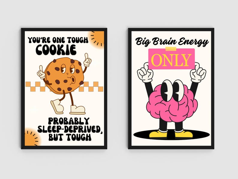 May include: Two framed art prints with black borders. One features a cartoon cookie with the text "YOU'RE ONE TOUGH COOKIE" and "PROBABLY SLEEP-DEPRIVED, BUT TOUGH." The other shows a cartoon brain holding a sign that says "ONLY" with the text "Big Brain Energy."