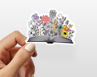 May include: A sticker of an open book with colourful flowers growing out of it. The book is grey and the flowers are pink, yellow, blue, purple, and green.