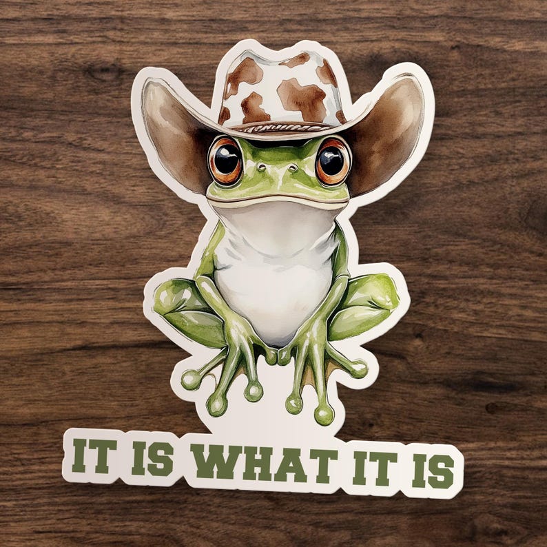 May include: A whimsical sticker featuring a green frog wearing a brown and white cowboy hat. The frog has large, expressive eyes and is sitting with its legs crossed. The text "IT IS WHAT IT IS" is printed in green below the frog.