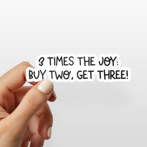 May include: White sticker with black text that reads "3 times the joy: buy two, get three!"