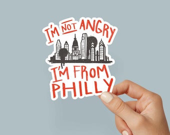 May include: A white sticker with red and black text that reads "I'm not angry I'm from Philly" with a black and white illustration of the Philadelphia skyline.